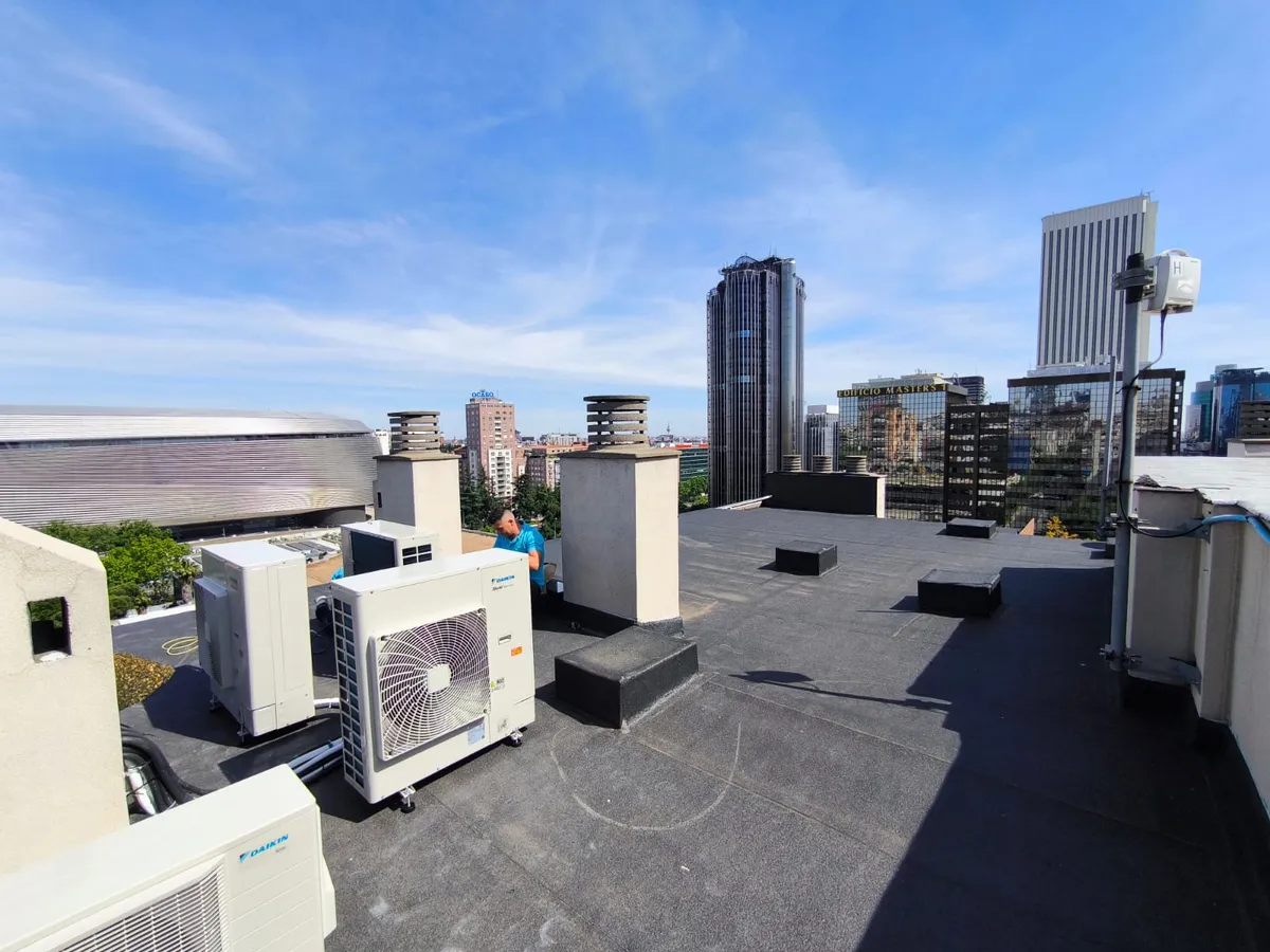 Batería de equipos de aire acondicionado instalados en una azotea con vistas al skyline de Madrid