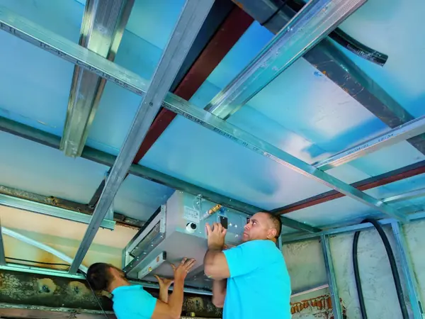 Dos instaladores de BioClima21 subiendo una unidad interior hasta la estructura del techo