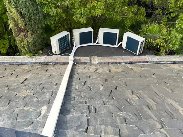 Cuatro unidades exteriores alineadas sobre la cubierta de pizarra de una vivienda, con la tubería protegida en canaleta