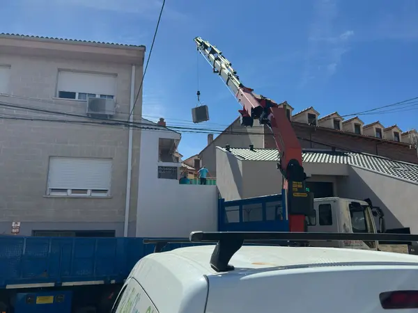 Grúa elevando la unidad exterior sobre la calle, con la furgoneta de BioClima21 en primer plano