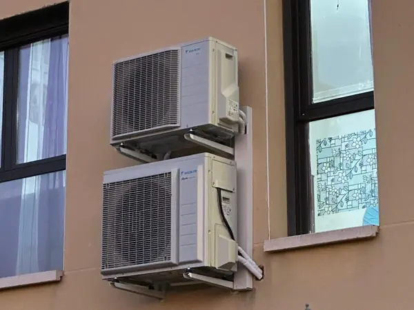 Dos unidades exteriores de aire acondicionado sobre soportes en la fachada, junto a una ventana