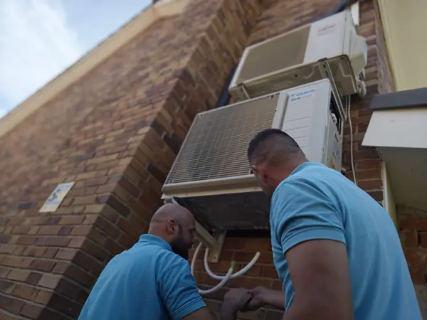 Dos técnicos de BioClima21 conectando las unidades exteriores montadas en una pared de ladrillo