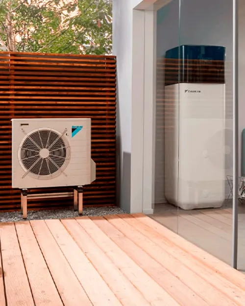 Unidad exterior de aerotermia Daikin en un patio y unidad interior junto al ventanal